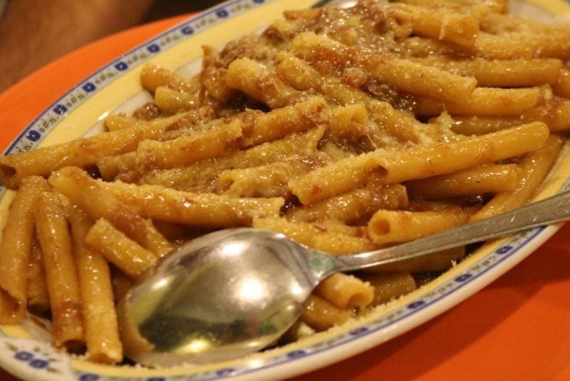 pasta tubes with a red ragu sauce and melted cheese on a white oval shape with blue flowers around the edges