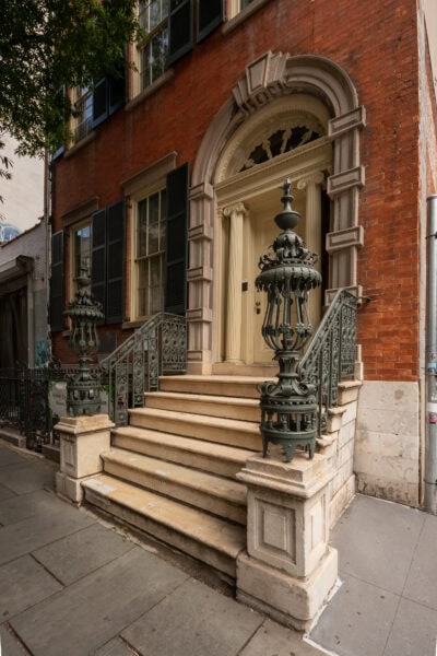 Stone steps leading to a cream front door with a stone arch around it in a tall red brick townhouse.