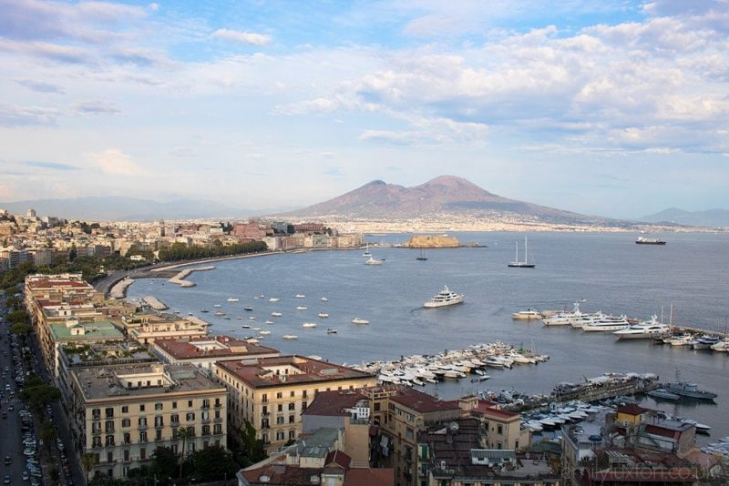 view of the harbour in Naples with Mount vesuvius across the bay and many yachts and smaller boats moored in the water. Best things to do in Naples. 