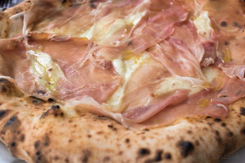 Close up of a pizza topped wit hthin slices of parma ham and cheese. Where to eat in Naples