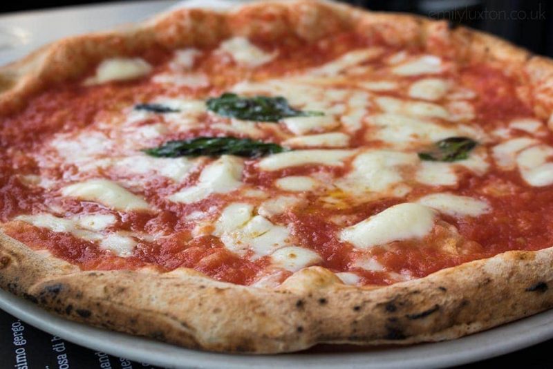 Close up of a pizza on a white plate with red sauce, mozarell acheese, and basil leaves. naples food guide