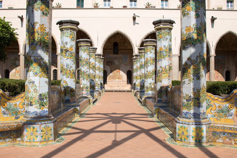 courtyard in a convent with orange tiled floor and a pathway lined by 6 blue columns on either side patterned with leaves and fruit