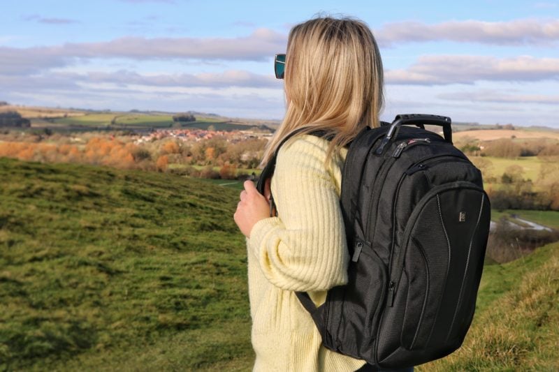 blonde girl in yellow jumper standing in field wearing a black travel backpack