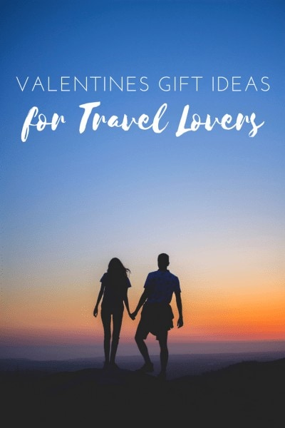 Unique Valentine's Gifts for Travel Lovers: written in white text on top of a photo showing a silhouette of a man and woman holding hands on top of a mountain with a sunset sky behind them.