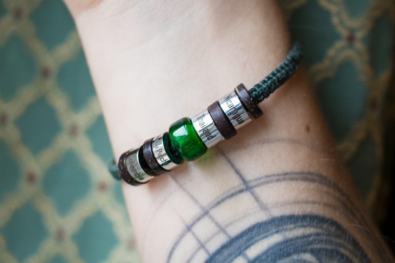 Close up of a wrist wearing a bracelet made from green rope with wooden and silver metal beads on it.