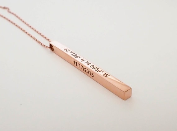 Close up of a rose gold necklace with a bar-shaped pendant engraved with coordinates and a date.