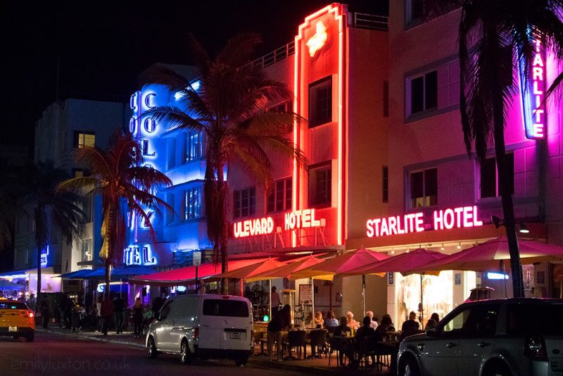bars on Miami Ocean Drive at night with neon signs in blue, red, and pink
