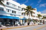 row of hotels on Ocean Drive in Miami, white and pastel yellow art deco buildings with a line of palm trees along the tarmac road in front. Facts about Miami.