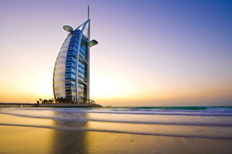the burj al arab at sunset in dubai - a curved tower with the sea in front