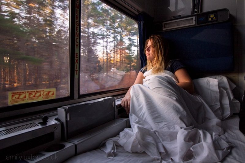 blonde girl wrapped in a white sheet on a sleeper train from New York to New Orleans looking out the window at some pine trees - amtrak crescent review