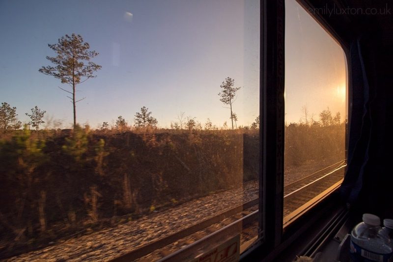 looking out a train window at a few trees and train tracks with the sun setting. On the 30 hour train from New York to New Orleans