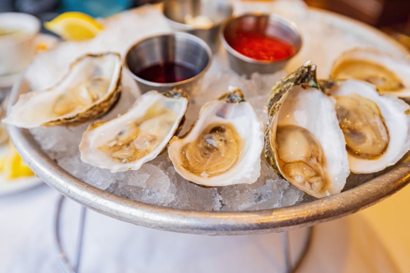 Close up shot of fresh raw Louisiana oysters on a bowl of ice with three small silver tubs of sauce at a restaurant in New Orleans