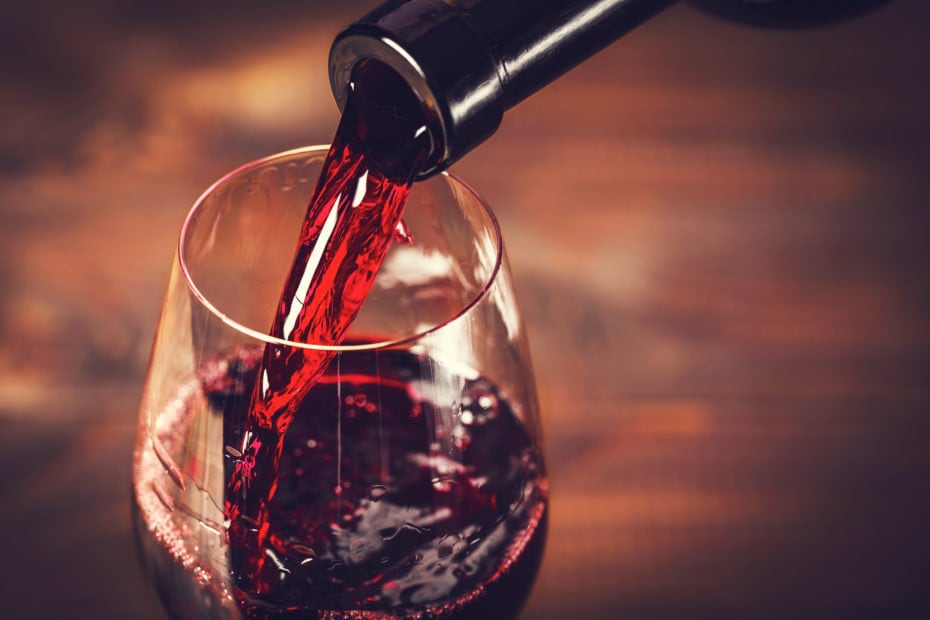 Pouring red wine into the glass against wooden background