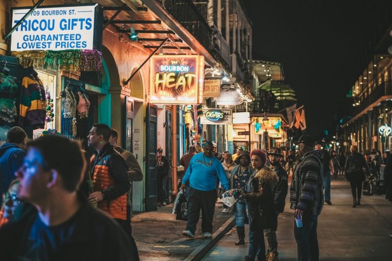 a busy street at night with several bars in a line and lots of lit up signs. new orleans food