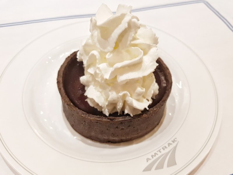 close up of a small circular chocolate tart and whipped cream on a small white plate. amtrak crescent review