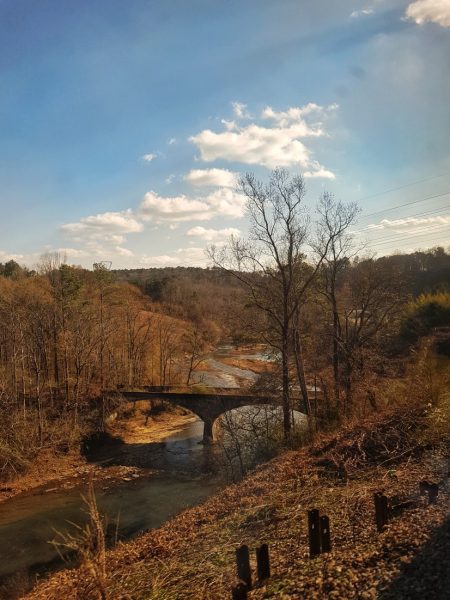 a small stone two tier bridge over a river in autumn with brown leaves and bare trees all around. View from the Amtrak Crescent train from new york to new orleans.