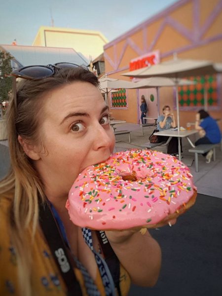 Selfie of Emily taking a bite of a pink doughnut with sprinkles the same size as her head outside a replica of Moe's Tavern at Simpson's Land in Universal Studios Florida