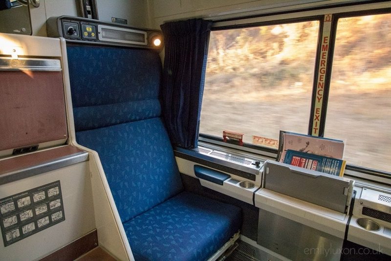 A blue train chair next to a large train window. Amtrak Crescent Viewliner Roomette Review