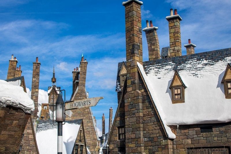 roofs of stone cottages with snow on them against a bright blue sky with a signpost pointing towards Hogwarts at the Wizarding World of Harry Potter in Florida