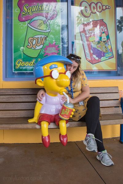 Emily wearing a bright yellow dress and black leggings hugging a statue of Millhouse from the Simpsons who is drinking from a can through a straw - how to do universal studios orlando on a budget