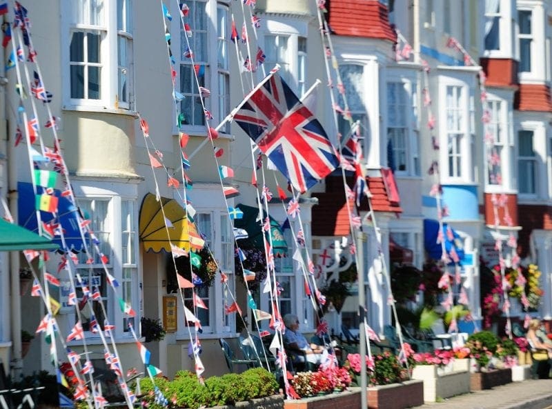 row of narrow terraced three-storey georgian houses painted cream covered in strings of flags and bunting with a union jack flying from the central house