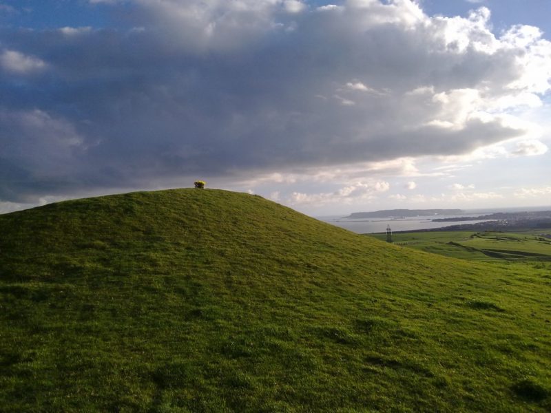 grassy mound on top of a hill with a view of the sea beyond on a cloudy day - a bronze age burial mound at bincombe bumps in Weymouth