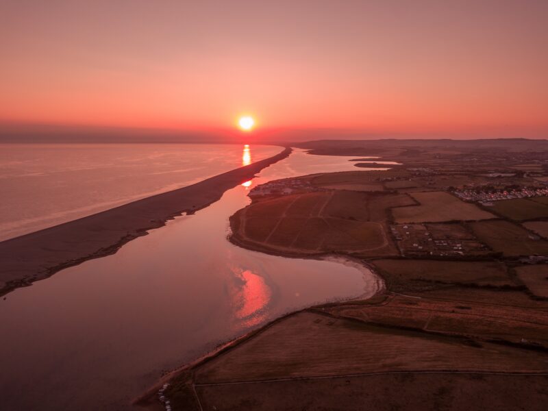 Lagoon next to a long thing beach with the sea on the other side at sunset with the mainland in silhouette
