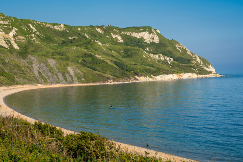 a shingle beach in a small bay towards a grassy headland