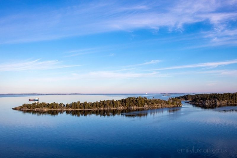 blue sea with small islands covered in green forest and a bright blue sky overhead sailing away from Stockholm harbour