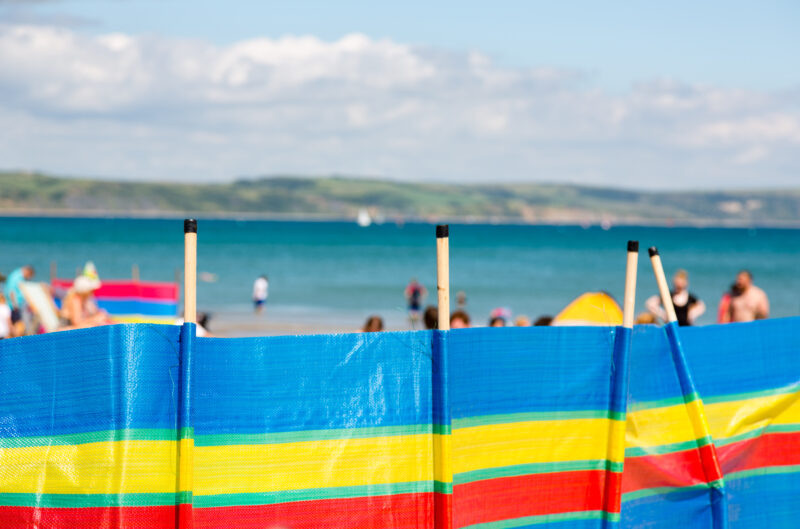 Striped windbreaker on beach in multicolors stripes, blue, green, yellow, red. Beach and see in blurred background.