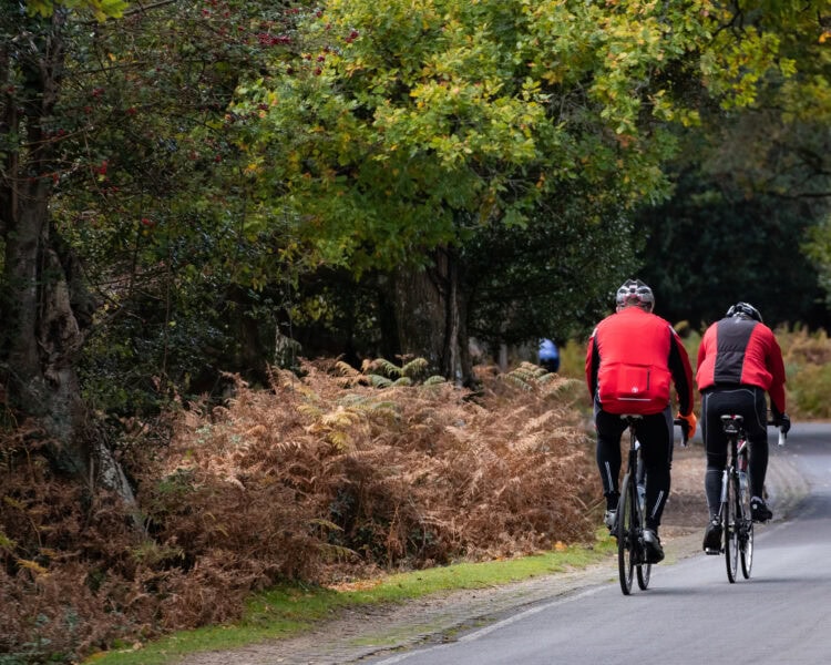 Two cyclists in red jackets on a country road next to a forest