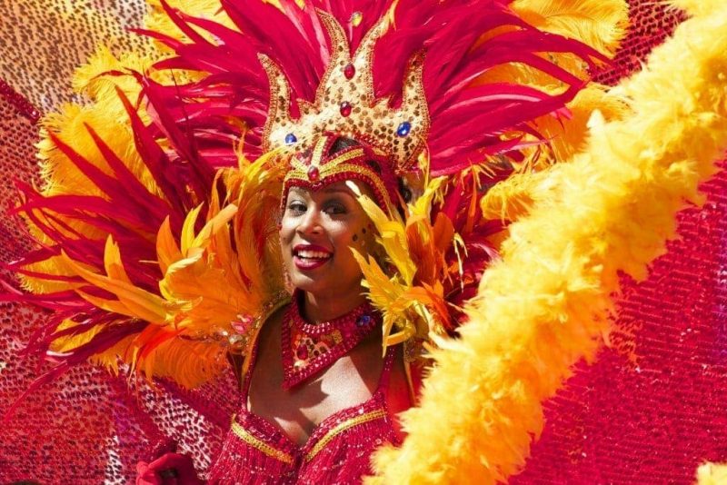 close up of a woman's hewad and sholders at Rio Carnival, she is wearing a red tassled bikini top and a large golden crown shaped headress surrouned by large red and yellow paper wings covered in sequins and yellow feathers. Rio Carnival is one of the best festivals around the world.