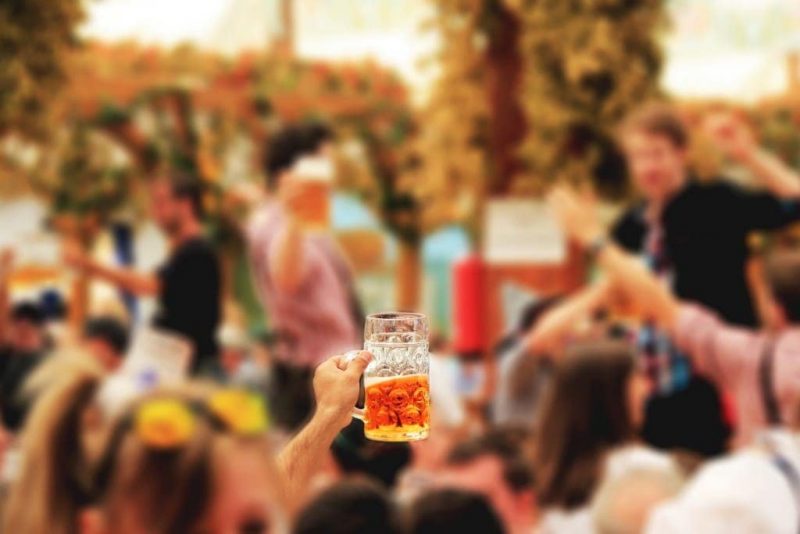 glass tankard of beer being held aloft above a crowd with only the hand and beer in focus at Oktoberfest in Munich festivals around the world.
