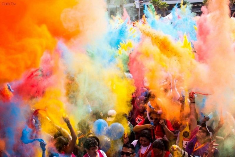 crowd of people beneath clouds of different coloured smoke and paint being thrown during Holi in India. Best Festivals Around the World.