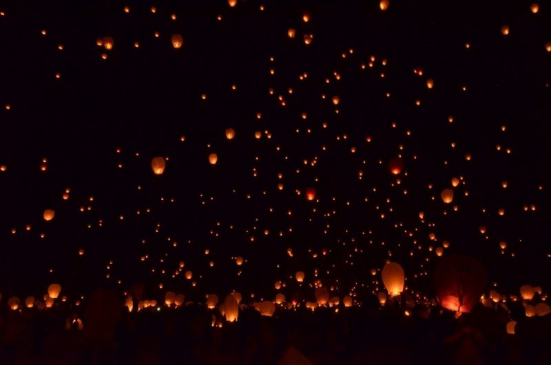 hundreds of paper lanterns with small candles inside floating in a dark night sky at Pingxi Lantern Festival