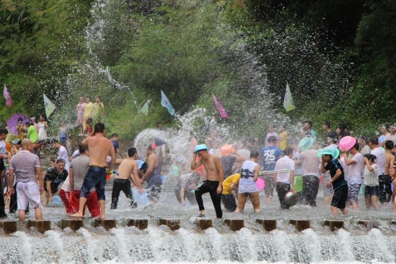 crowd of thai people in a river holding coloured buckets and throwing water at one another with a green leafy forest behind them at songkran festival in Thailand. festivals around the world.