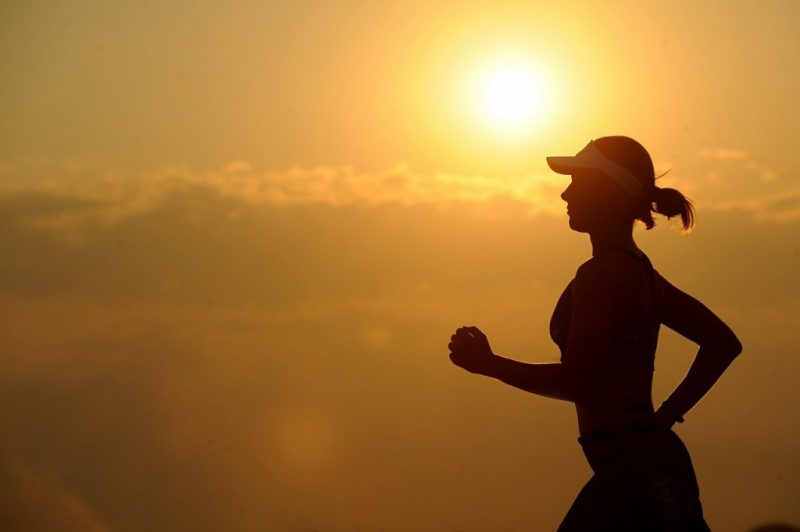 Woman in silhouette against a sunset wearing a visor and running. Best running app for beginners.