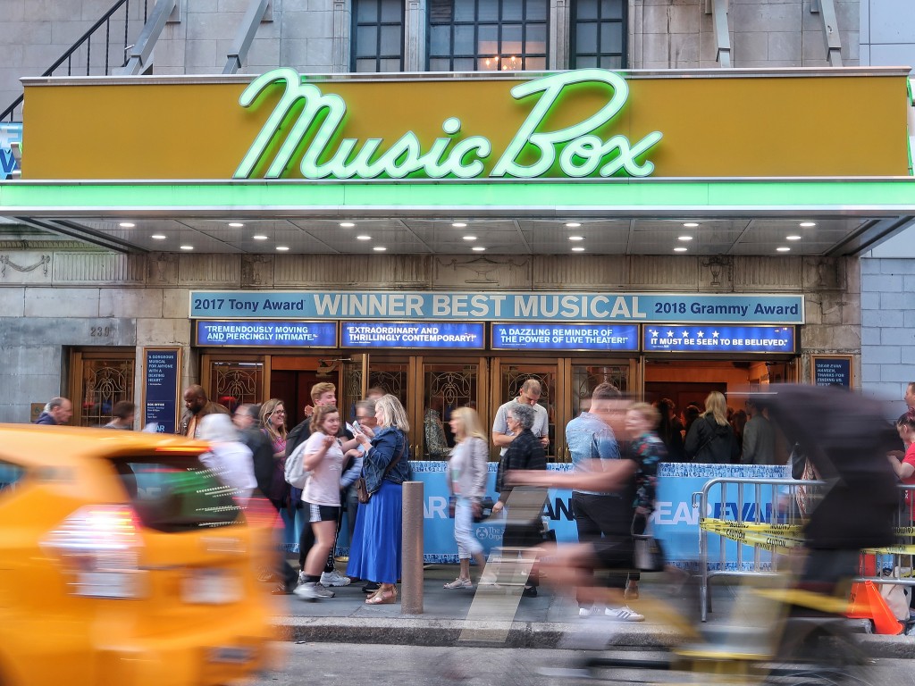 Busy street with a blurred taxi and people in front of the Music Box theatre with the name written in green neon letters on a yellow background