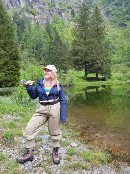 Girl fly fishing in waders by a lake