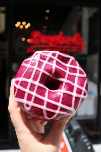 close up of a hand holding a purple doughnut with crisscrossed pink icing - dessert NYC