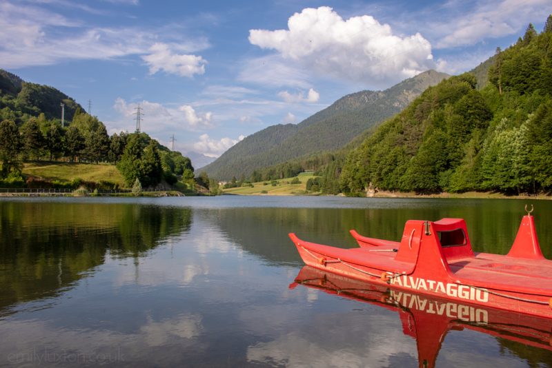 a red boat on a still lake betwen mountains in trentino italy, a popular setting for walking holidays