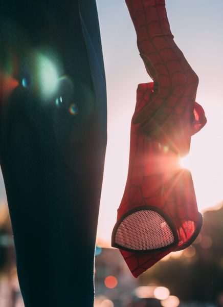 close up of a person's leg and hand in a spiderman costume holding the mask in a gloved hand with the sunset behind