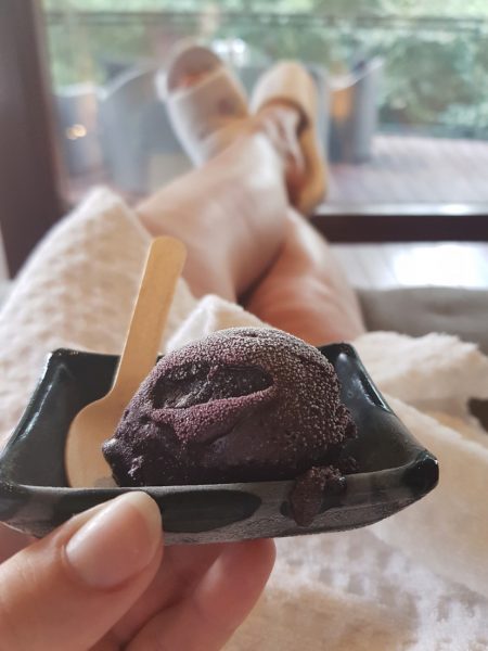 Emily's hHand holding a small bowl of chocolate ice cream aboveher lap with her legs crossed on the couch in front of her, Emily is wearing a white dressing gown and white spa slippers, at Seaham Hall Spa in County Durham UK