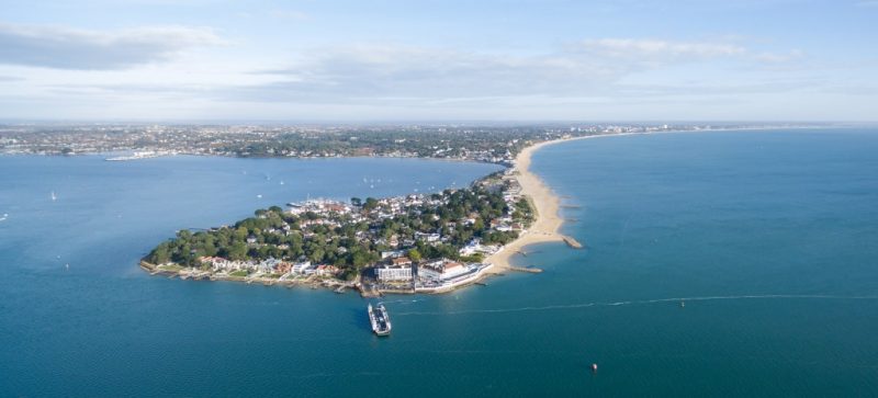 aerial view of a small peninsula connected to the mainland by a long sandy beach 