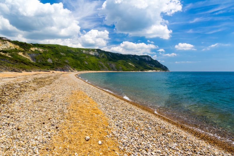 looking along a shingle beach in a small bay towards a grassy headland 