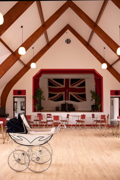 Vintage cream and black pram in a village hall with wooden floor and a stage with a large union jack flag above it - the Fifties Welfare Hall at Beamish Museum in Durham