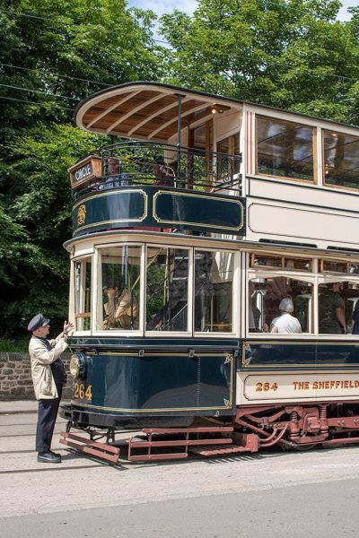 Historic double decker tram painted in dark green and cream with the conductor standing in front wearing a cream jacket and navy blue cap. Things to do in County Durham UK