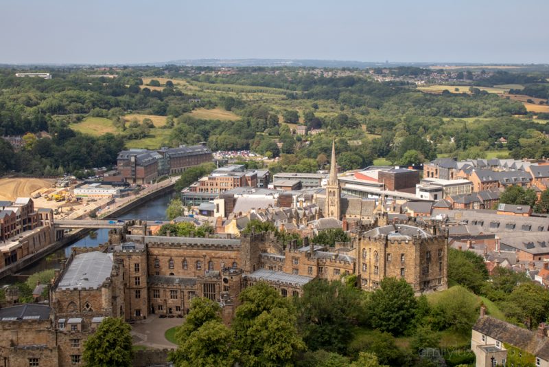View of Durham city skyline from the top of the Cathedral tower, the city centre is small with the light brown stone castle in front and a church tower rising in the middle, and beyond the city are grassy fields and hills and typical english countryside. Most beautiful cities in England.