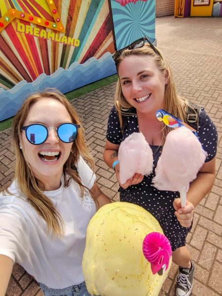 Two girls eating candyfloss at funfair