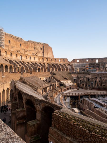 Inside the Colosseum in Rome in January - ruined orange stone walls in a circle with clear blue sky above